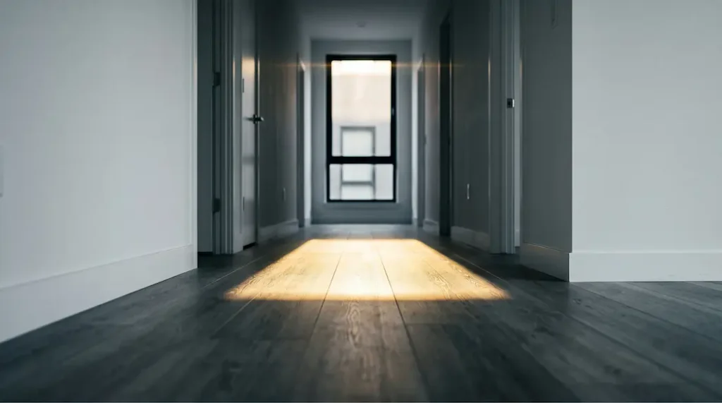 Empty rental apartment hallway with SPC flooring catching sharp afternoon light before tenant move-in