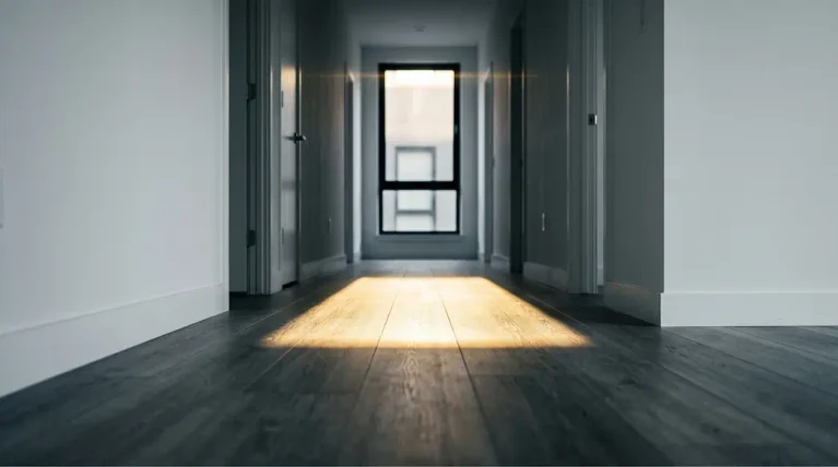 Empty rental apartment hallway with SPC flooring catching sharp afternoon light before tenant move-in